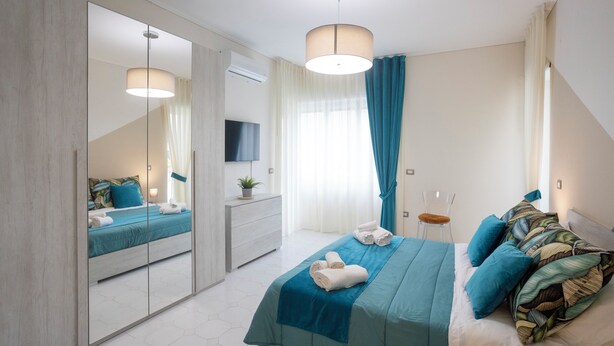 A modern bedroom with a large mirror, a bed with blue bedding, a dresser, and a television. - Apartment within walking distance of downtown and the sea (Sorrento)