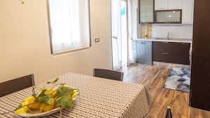 A dining area with a table set for two, a kitchen in the background, and a view of the outside through a door. - Apartment within walking distance of downtown and the sea (Sorrento)