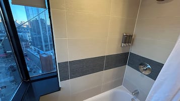 A modern bathroom with a bathtub, a shower, and a window offering a city view.