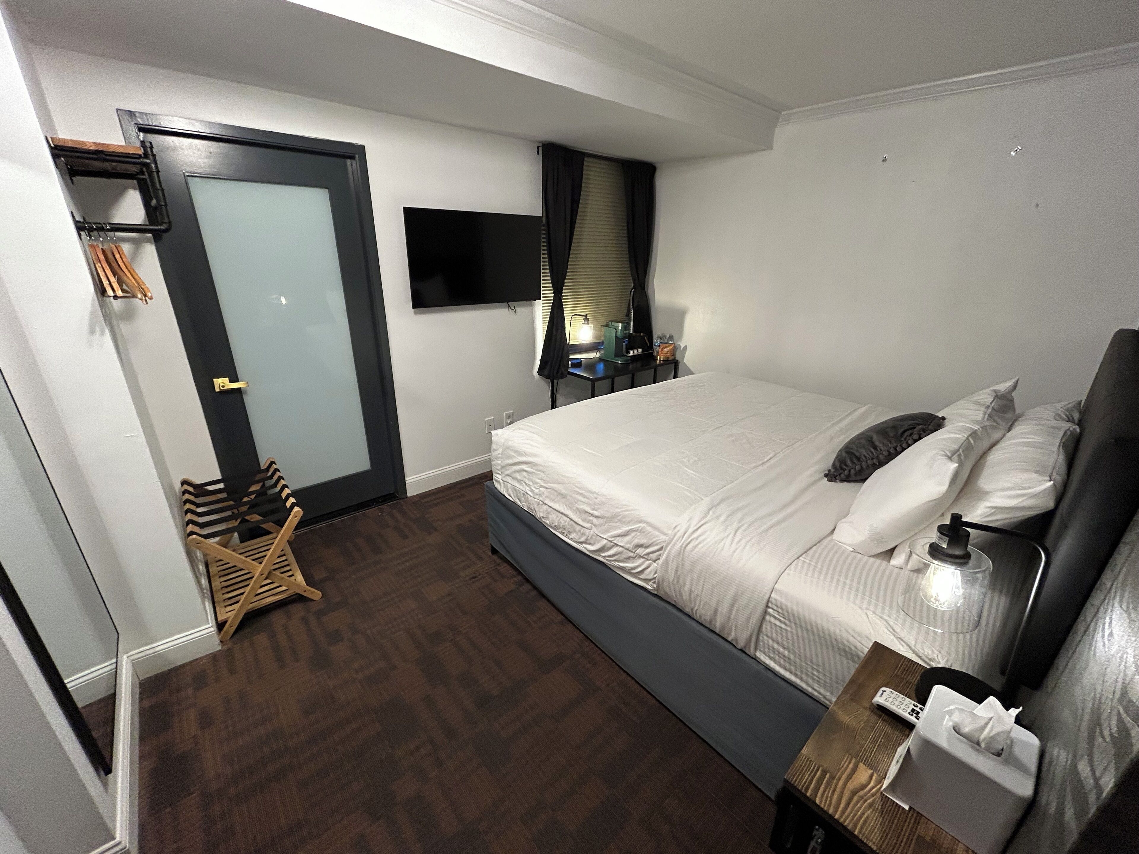 Habitación de hotel con cama, televisor, mesita de noche, silla y puerta.