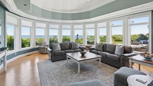 Ein geräumiges Wohnzimmer mit großem Erkerfenster und Meerblick, ausgestattet mit Ledersofas und einem Couchtisch.