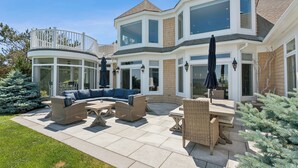 Ein großes, modernes Haus mit einer geräumigen Terrasse, die mit Gartenmöbeln ausgestattet ist und ein großes Fenster mit Blick auf den Garten hat.