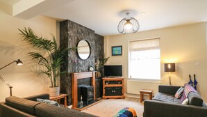 A living room with a fireplace, sofa, TV, and a large window. - Globe Cottage (Weymouth)
