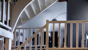 Un interior moderno con una escalera en espiral, barandillas de madera y una pared de acento oscura.