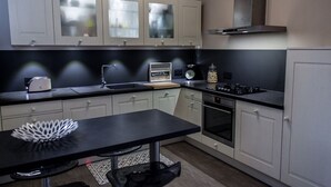 Una cocina moderna con armarios blancos, encimera negra, extractor de acero inoxidable y horno empotrado.