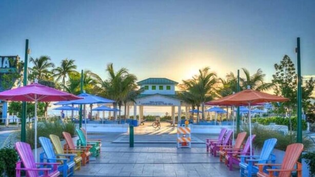 A resort area with colorful Adirondack chairs and umbrellas, a covered seating area, and palm trees. - Sea Star Suites By The Sea #7 Steps 2 Beach & Pubs (Lauderdale-by-the-Sea)