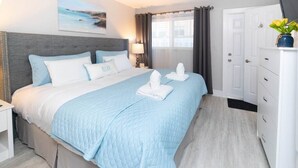 Una habitación de hotel con cama, mesita de noche, lámpara, ventana con cortinas, puerta y un armario con un florero.