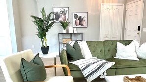 A modern living room with a green sofa, a wooden chair, a white table, and a potted plant. - Relaxing 3BED 2BATH POOL Home w. Pond View & HOT TUB (Brandon)