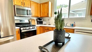 A kitchen with wooden cabinets, stainless steel appliances, a coffee maker, and a potted plant on the counter. - Relaxing 3BED 2BATH POOL Home w. Pond View & HOT TUB (Brandon)