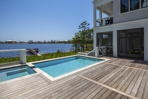 A swimming pool with a wooden deck, a balcony with outdoor furniture, and a view of the water. - Lakefront, Private Pool, Walk to beach, shops and restaurants, 30A Bike Path (Santa Rosa Beach)