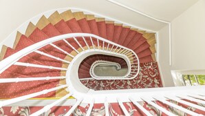 A spiral staircase with a red and beige patterned carpet, white balusters, and a central glass panel. - LOGIS HOTEL DU PARC (Pont-a-Mousson)