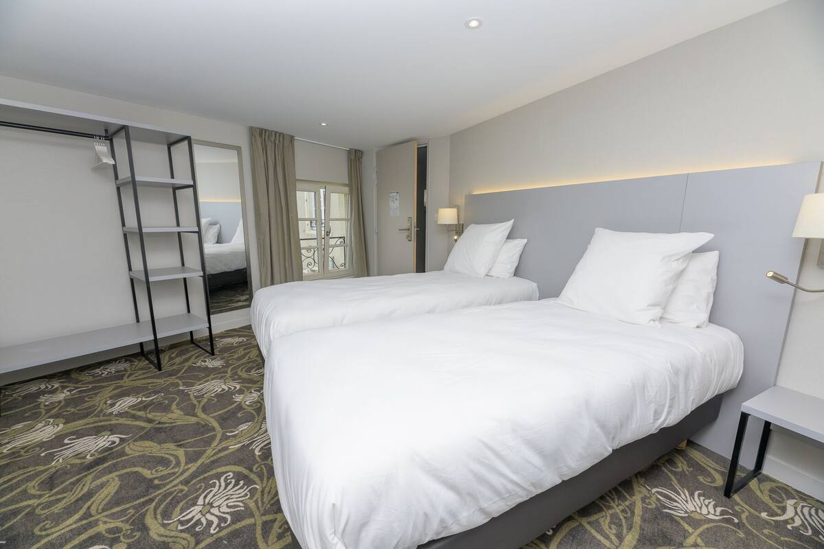 A hotel room with two beds, a wardrobe, a mirror, a bedside table, and a patterned carpet.