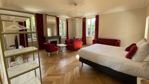 A hotel room with a large bed, a fireplace, a red armchair, a small table, and a mirror. - LOGIS HOTEL DU PARC (Pont-a-Mousson)