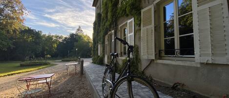 A building with a bicycle parked outside, a table and chairs, and a garden area.