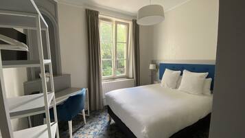 A hotel room with a bed, a desk, a chair, a window, and a staircase.