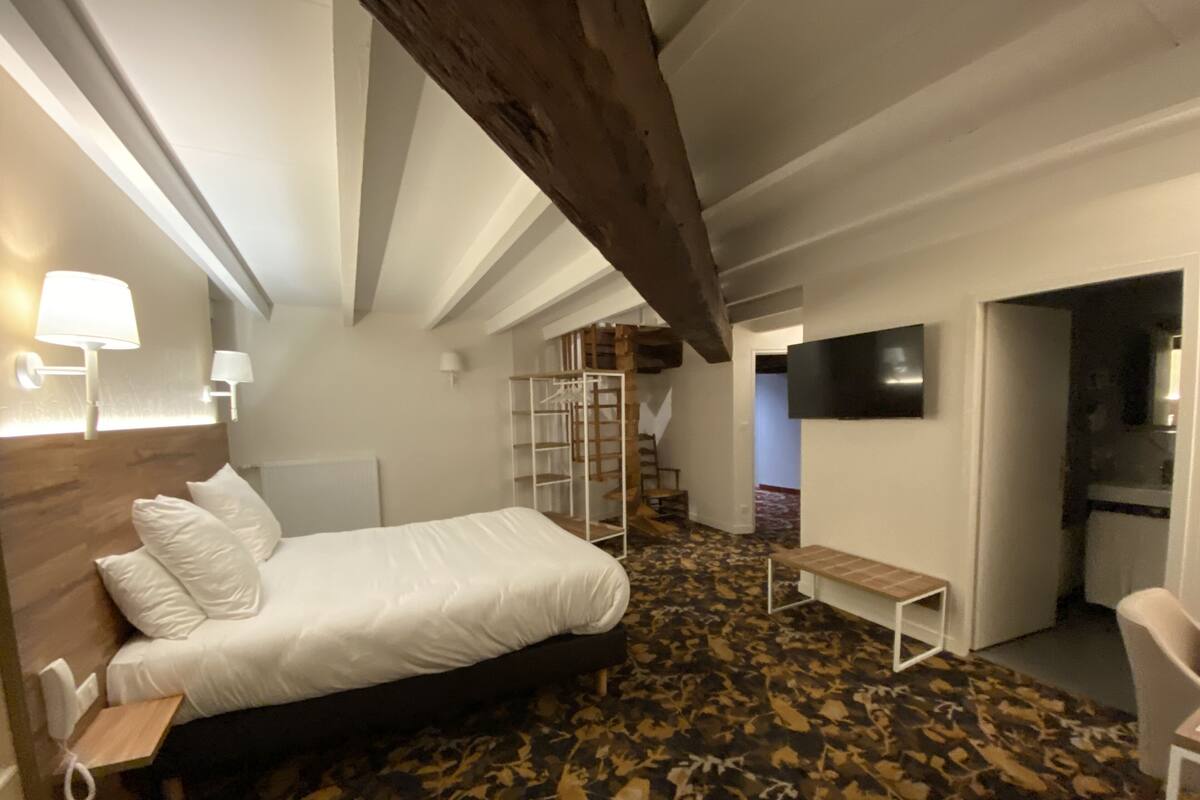 A bedroom with a bed, bedside table, lamp, and a TV mounted on the wall.