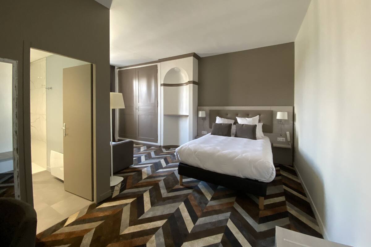 A modern hotel room with a large bed, a walk-in closet, and a herringbone-patterned floor.