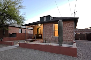 A single-story brick house with a covered porch and a cactus in the front yard.