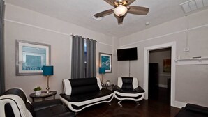 A modern living room with a ceiling fan, two black and white sofas, a TV mounted on the wall, and a large window with curtains.