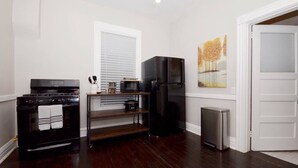 A compact kitchen with a stove, microwave, refrigerator, and a small trash bin.