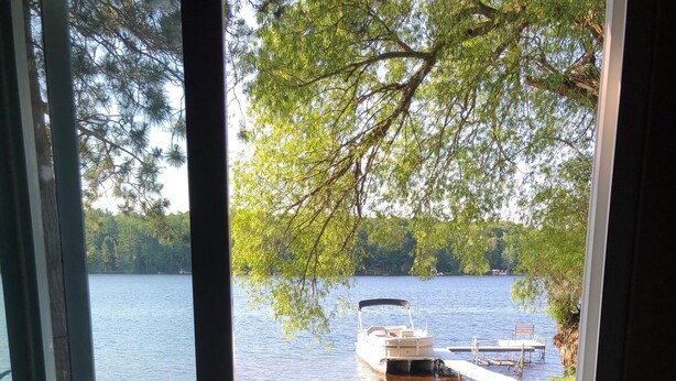 Näkymä lasiovesta, josta avautuu näkymä ruohikkoiselle alueelle, jossa on laituri ja järvellä oleva vene.