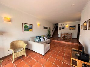 A living room with a sofa, a wicker chair, a dining table with chairs, and a staircase leading to another level.