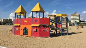 Un’area giochi sulla spiaggia con una struttura simile a un castello, comprensiva di scivoli e elementi da arrampicata.