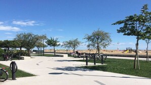 Un parco con vialetto lastricato, biciclette, alberi e un'area giochi sullo sfondo.
