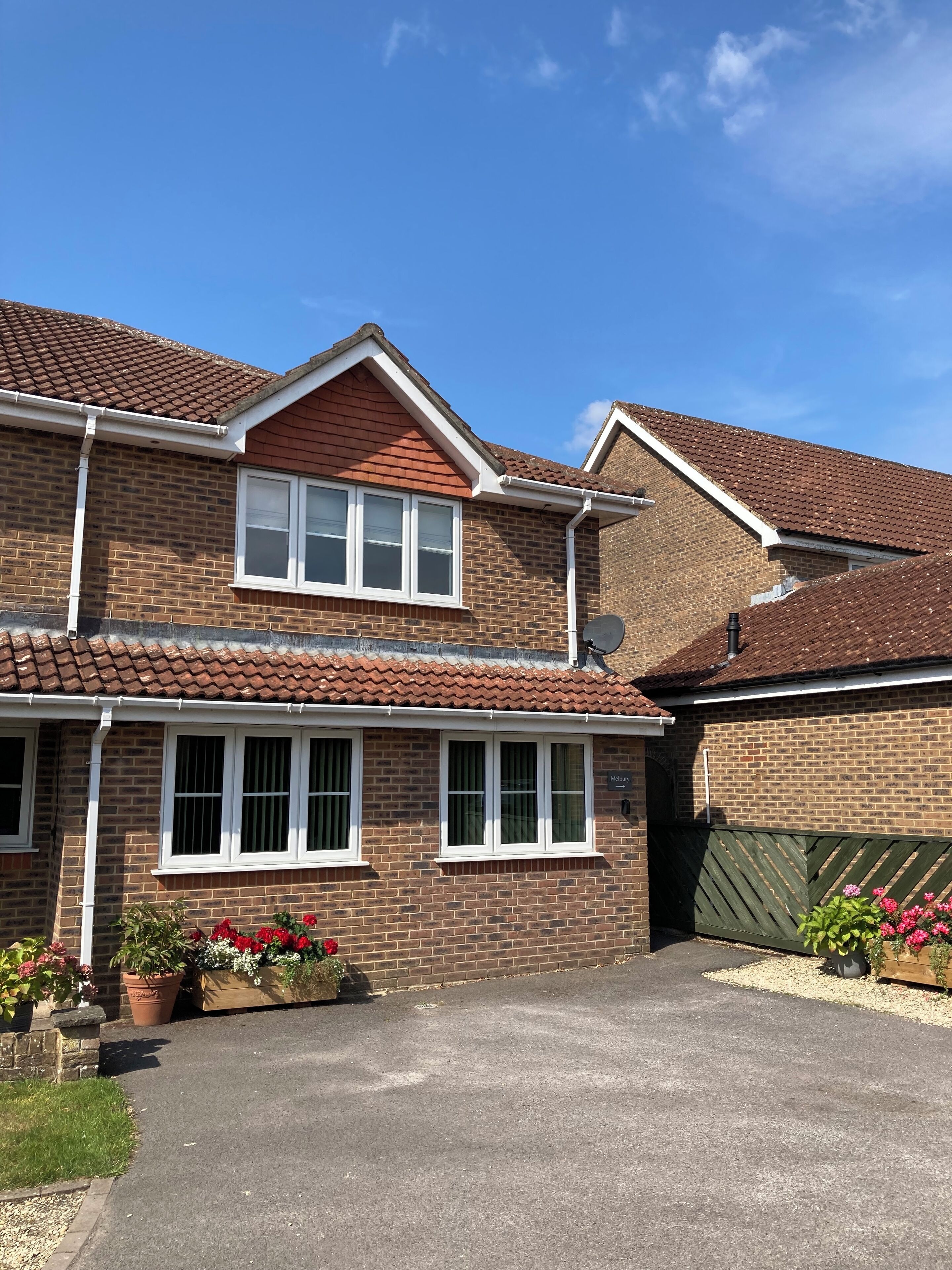 A two-story brick house with a tiled roof, a front garden with potted plants, and a driveway.