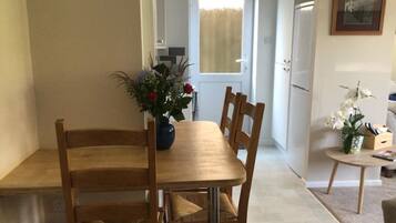 Zona pranzo con tavolo e sedie in legno, un vaso con fiori e una porta che conduce in un'altra stanza.
