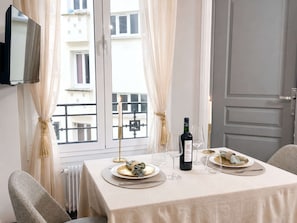 A dining table set with plates, a bottle of wine, and glasses, with a view of buildings through a window.