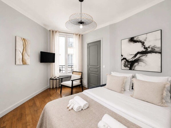 Una habitación de hotel moderna con cama, sillón, una mesita, televisión y obras de arte en las paredes.