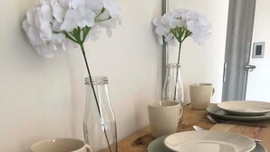 Ein Esstisch, gedeckt mit Tellern, einer Glasflasche und einer Vase mit weißen Blumen.