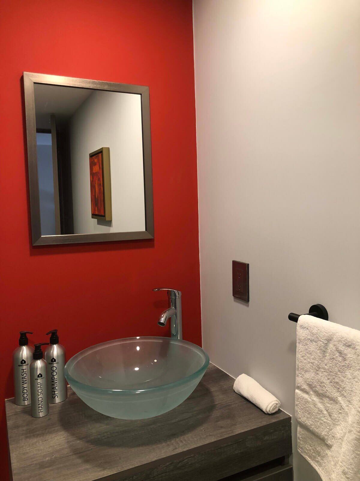 A bathroom with a glass sink, red walls, and a mirror.