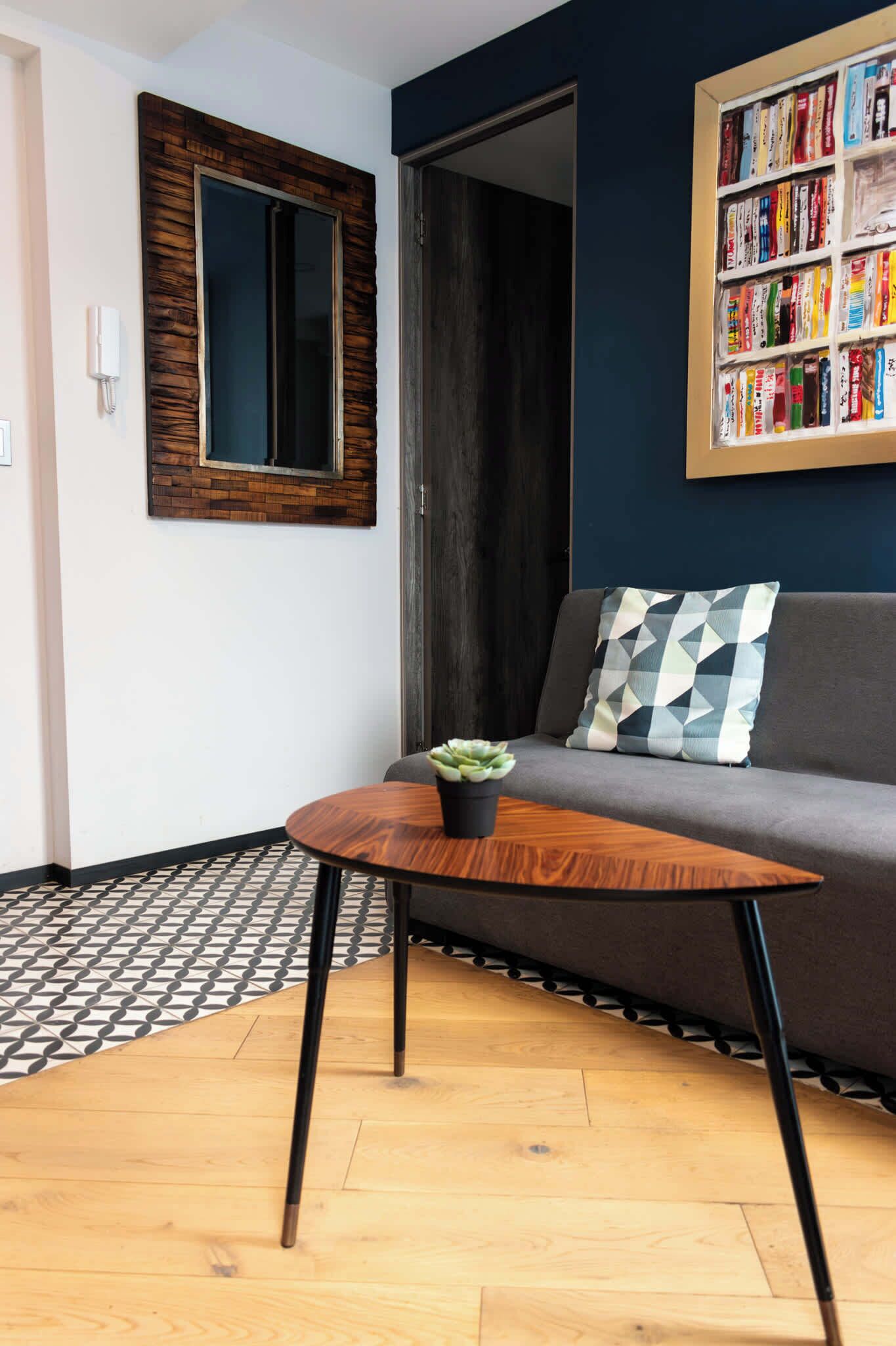 A modern living room with a dark blue wall, a bookshelf, a grey sofa, and a small wooden coffee table with a plant.