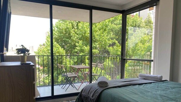 A bedroom with a large window, a bed, a wooden dresser, and a balcony with a table and chairs. - Excelente Apto con Terraza Pegado a la Condesa (Ciudad de México)