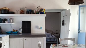 Cocina compacta con armarios blancos, zona de comedor con mantel floral y lámpara colgante.