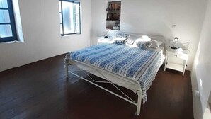 Un dormitorio con cama, mesitas de noche, una ventana y una estantería.