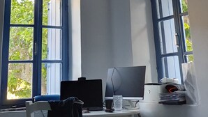 Una habitación con escritorio, computadora y dos ventanas con contraventanas azules.