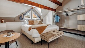 Ein Schlafzimmer mit einem großen Bett, Holzboden, einem Fenster, einem Nachttisch und einer Kleiderstange.