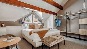 A bedroom with a large bed, a wooden ceiling, a window, a bedside table, and a hanging clothes rack.