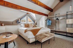 A bedroom with a large bed, a wooden ceiling, a window, a bedside table, and a hanging clothes rack. - Iskö Chalets-hötel (Eaux-Bonnes)