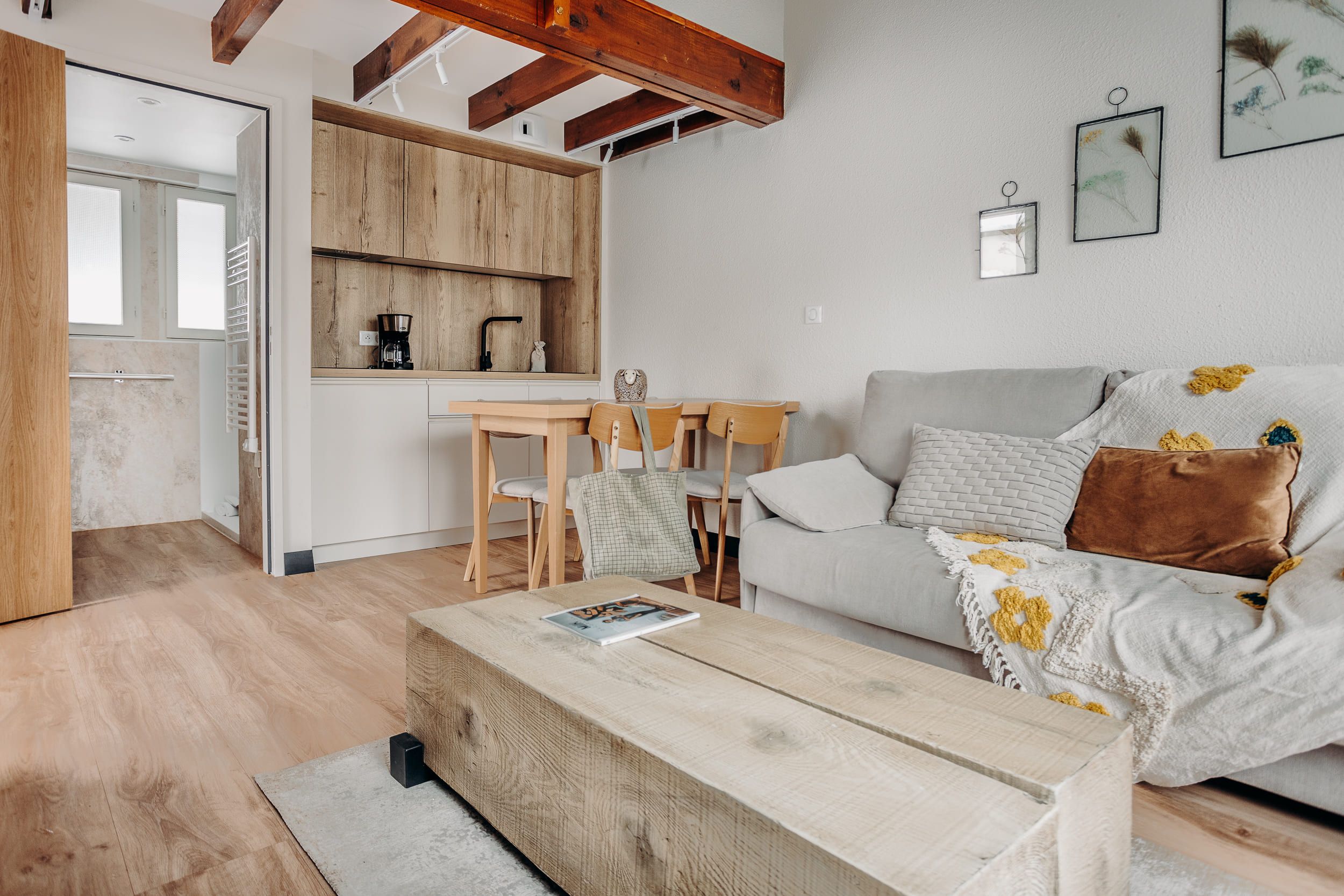 A modern living room with a wooden coffee table, a grey sofa with floral cushions, and a wooden dining table with chairs.