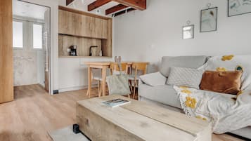 A modern living room with a wooden coffee table, a grey sofa with floral cushions, and a wooden dining table with chairs.