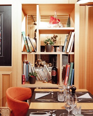 A dining area with a wooden table set for two, a bookshelf with books and decorative items, and a small Christmas tree. - Iskö Chalets-hötel (Eaux-Bonnes)