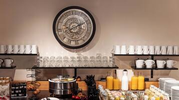Ein Frühstücksbuffet mit einer großen Wanduhr, verschiedenen Frühstücksangeboten und ordentlich angerichteten Tassen und Bechern.
