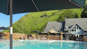 Ein Poolbereich mit Holzterrasse, Liegestühlen und Sonnenschirmen.