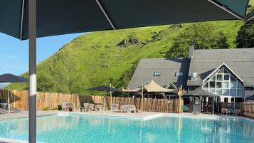 A pool area with wooden deck, lounge chairs, and umbrellas.