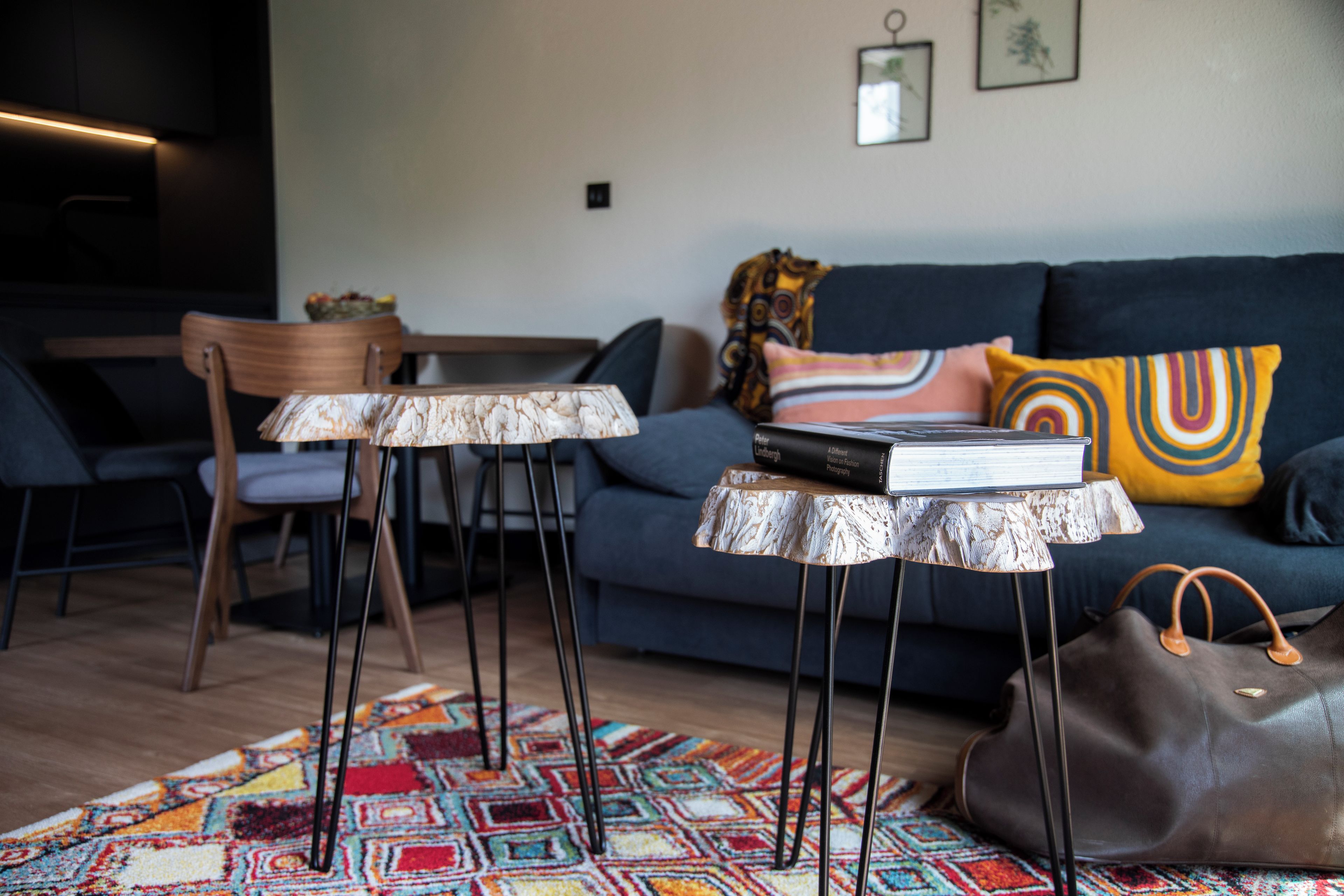 Ein Wohnzimmer mit einer Couch, einem Couchtisch, einem Sessel, einem gemusterten Teppich und einer Handtasche.