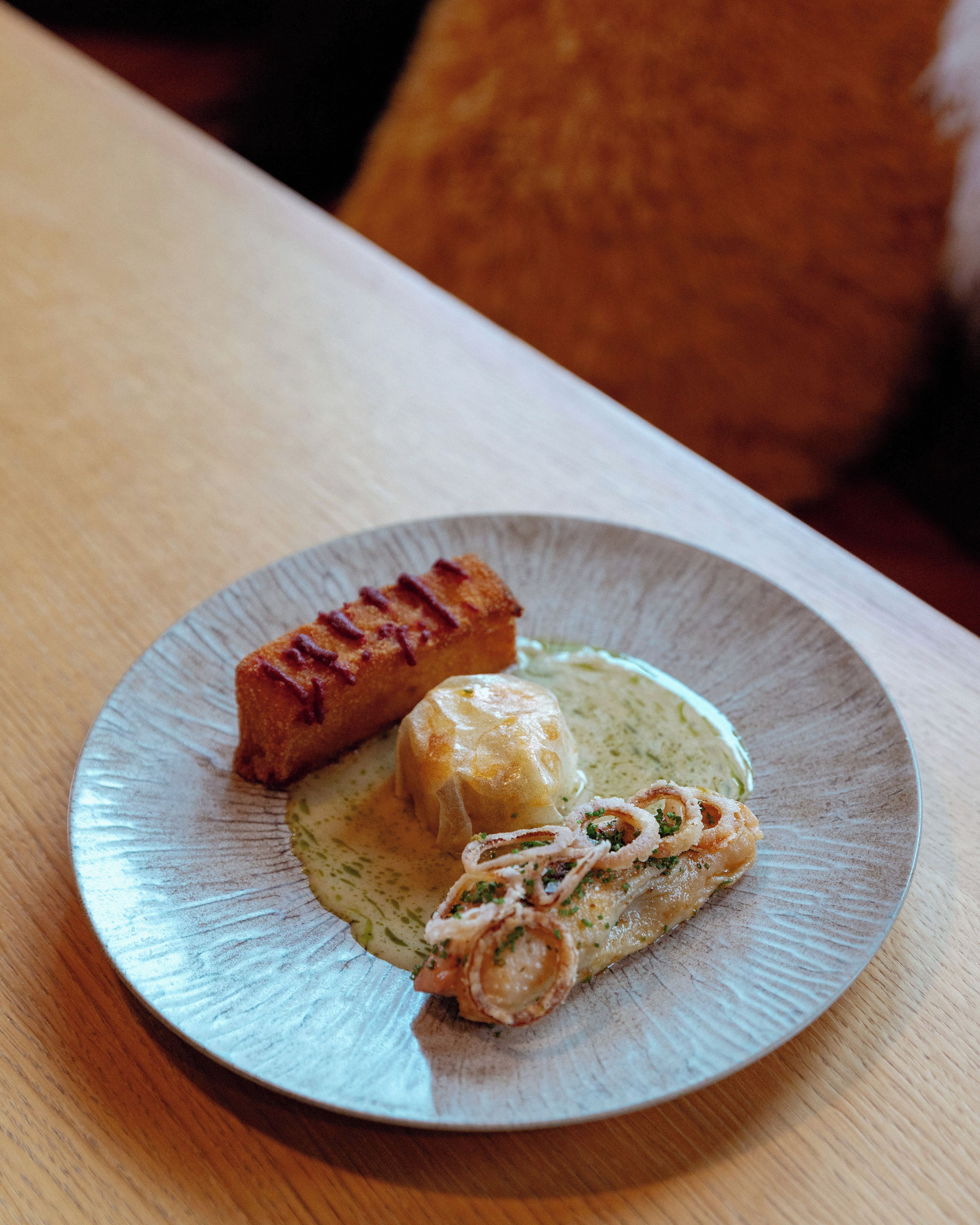 A plate with a piece of grilled meat, a dumpling, and a rolled omelette on a ceramic plate.